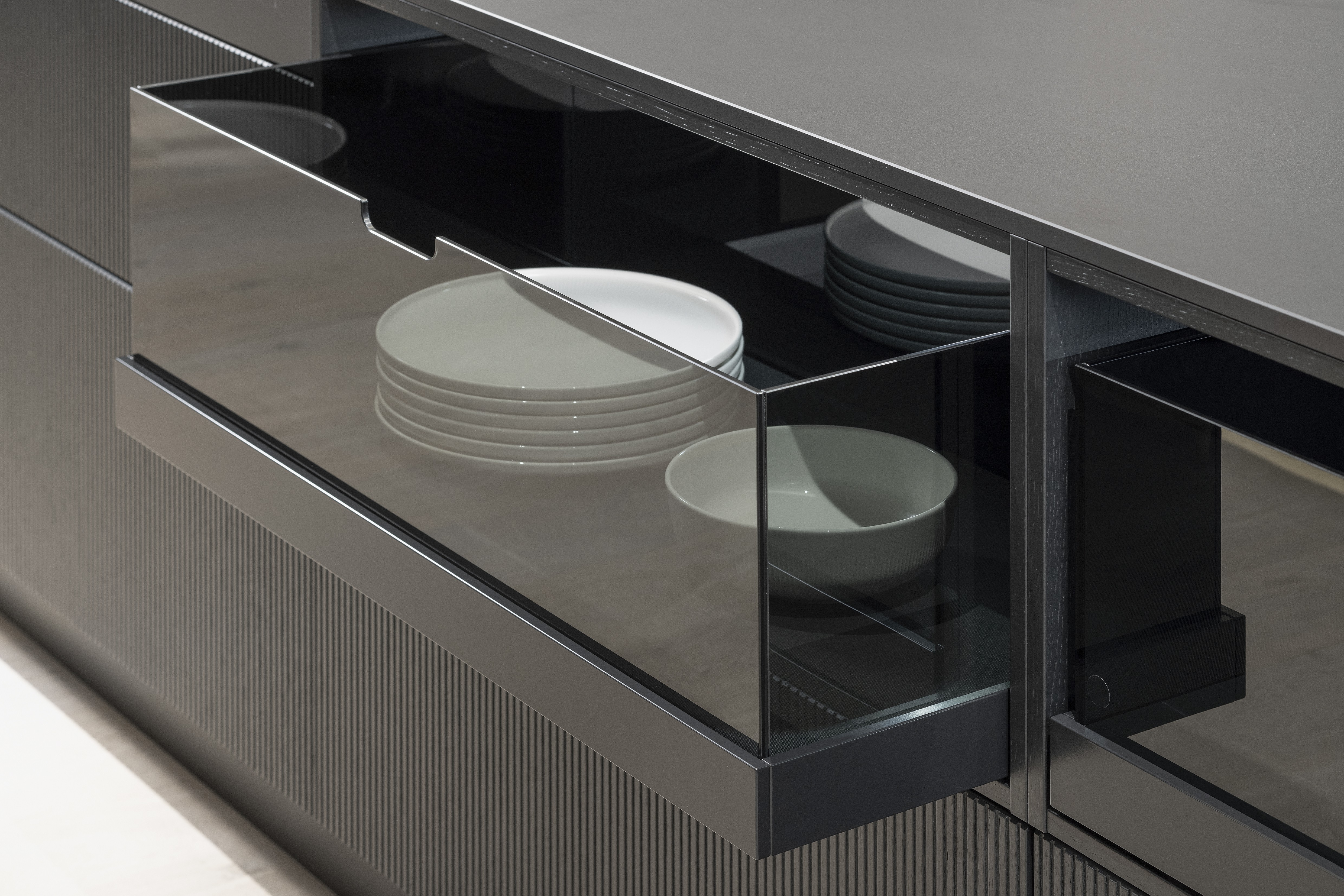 APL: Silk Negro Naturale (Keramik) 16 mm   Front: AV 6023-GL Eiche-schwarz Echtholzfurnier Rille AV 7070 Industriestahl Bronze, Metalliclack Korpus: 4059 Titan Griff: Kehlleiste 355 Schwarz matt Geräte: Miele Armatur: Gessi Features: Regalwandlösung mit beleuchtetem Wandboard, Oberfläche von Hand bearbeitet, Materialmix, Trendthema Bronze, Glasschublade mit Plexiglas in Schwarz getönt, Thekenlösung mittig, Wand aus Oberflächenmaterial in Bronze mit beleuchteten Funktionsleisten für Gläser, etc. 