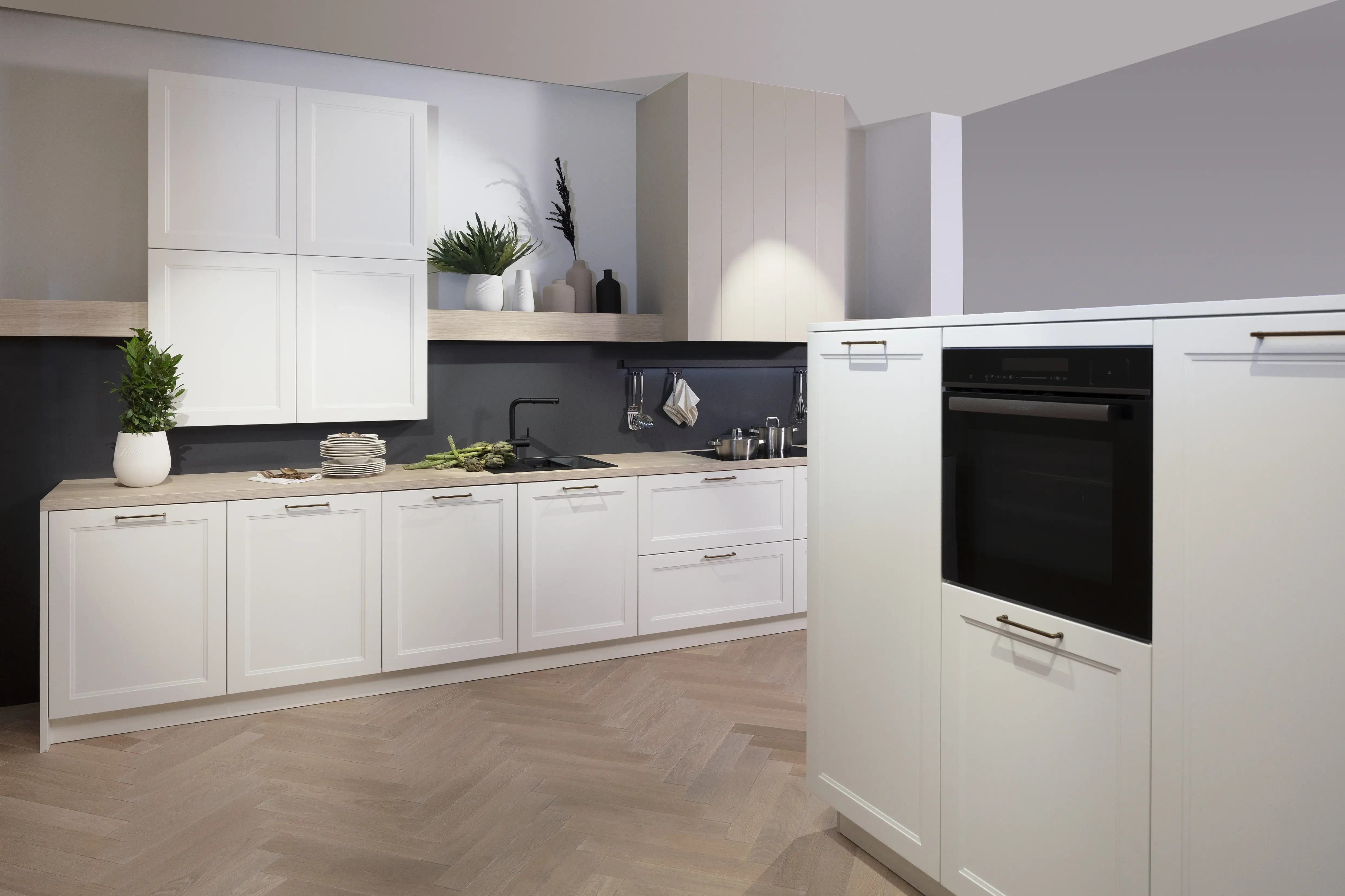 Moderne weiße Küche mit Einbaugeräten und Holzfußboden, dekoriert mit Pflanzen.